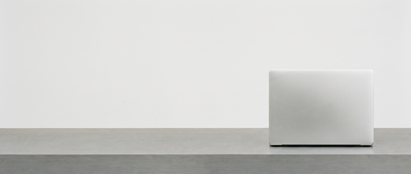 A single closed laptop alone on a long empty desk in a white studio